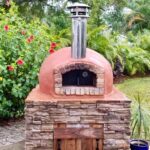 Forno Nardona Rustico Oven with terracotta colored stucco finish on a custom built base with black oven door and wooden base door.