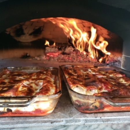 Lasagna sitting cooked inside a wood-fired pizza oven with a brick dome interior