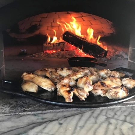 Chicken wings being cooked in a Forno Nardona oven on a flat cast iron pan.