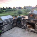 The Nardona Rustico is one of four models of Forno Nardona residential pizza ovens on a stoned base with granite countertop and a grand back yard view.
