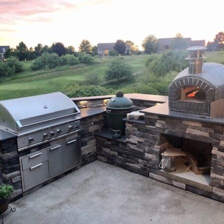 The Nardona Rustico is one of four models of Forno Nardona residential pizza ovens on a stoned base with granite countertop and a grand back yard view.