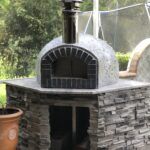 Forno Nardona Rustico oven with black firebrick face on corner stoned base with granite countertop.