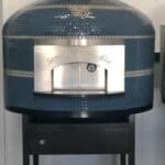 Blue tiled Napoli Oven by Forno Nardona with gray striping and black grout positioned on a Forno Nardona black powder coated stand with gas burner installed.