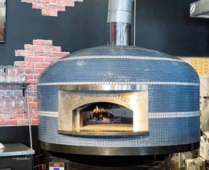 Blue glass tiled Commercial Nardona Napoli oven with white stripes and personalized face plate that says, "Let's Go Bolts!" It sits on a custom black stand and has an automatic gas burner.