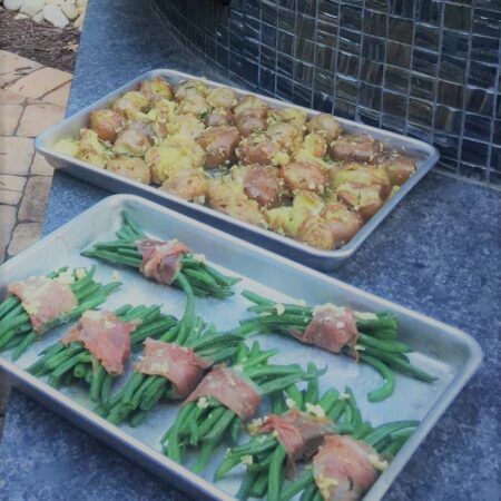 Two trays of food. One with golden garlic potatoes with skin and the other with prosciutto wrapped green beans ready to go in the Nardona Napoli oven.