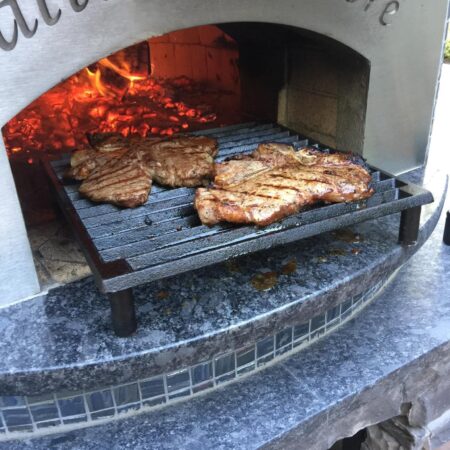 Two deliciously looking steaks on a rack at the front of a Forno Nardona Napoli oven.