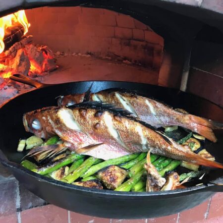 Two hole fish scored and cooked on a bed of asparagus in a round cast iron pan in a Forno Nardona oven.